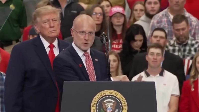 President Trump stands beside a man speaking at the presidential lectern at his rally in Wasilla, Alaska, October 13, 2026 (still from Rapid Response 47 video)