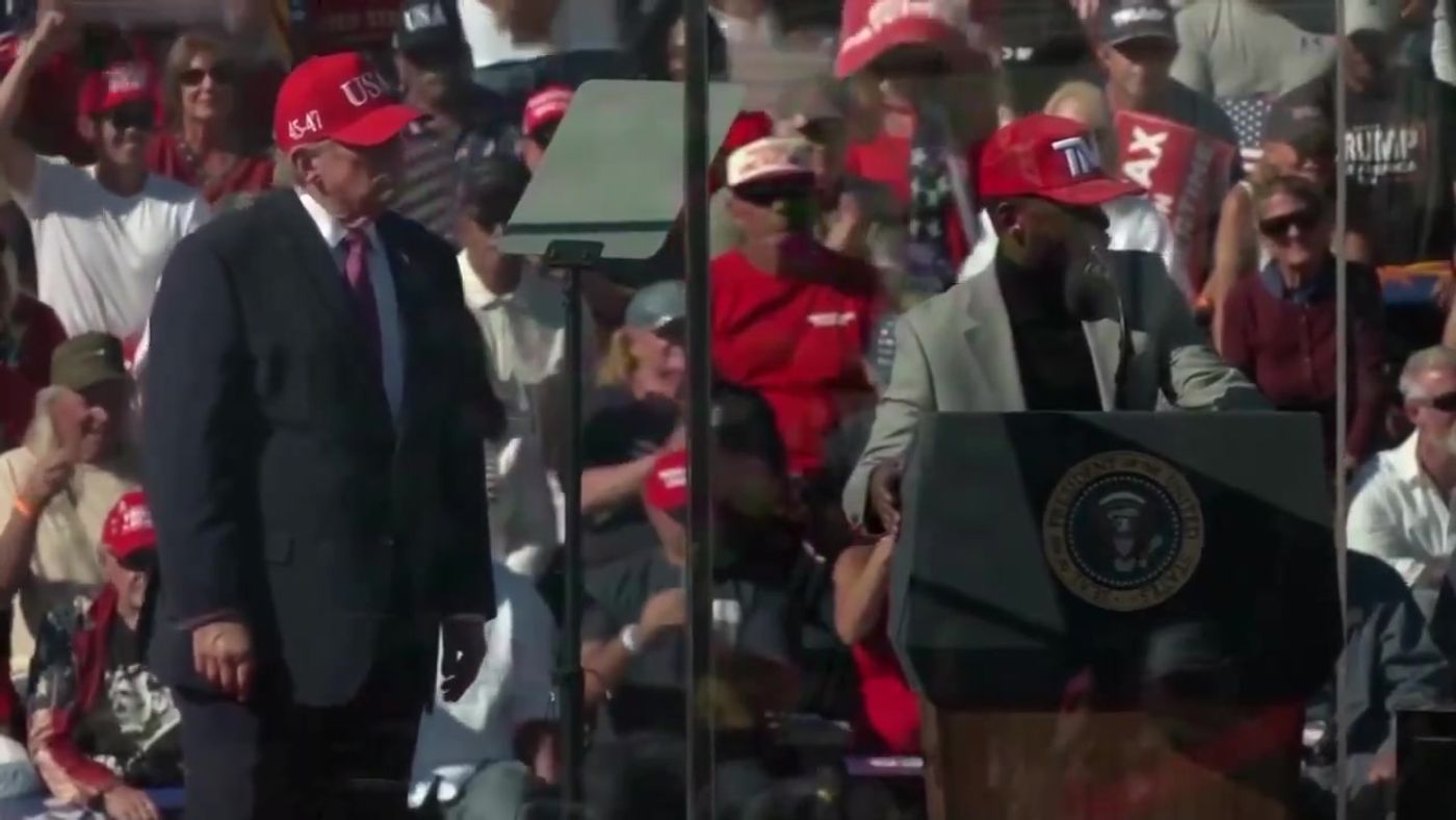 Boxing legend Floyd Mayweather speaks at the Presidential Seal podium as President Trump stands beside him on stage at the Bullhead City, Arizona rally, October 14, 2026 (still from Rapid Response 47 video)