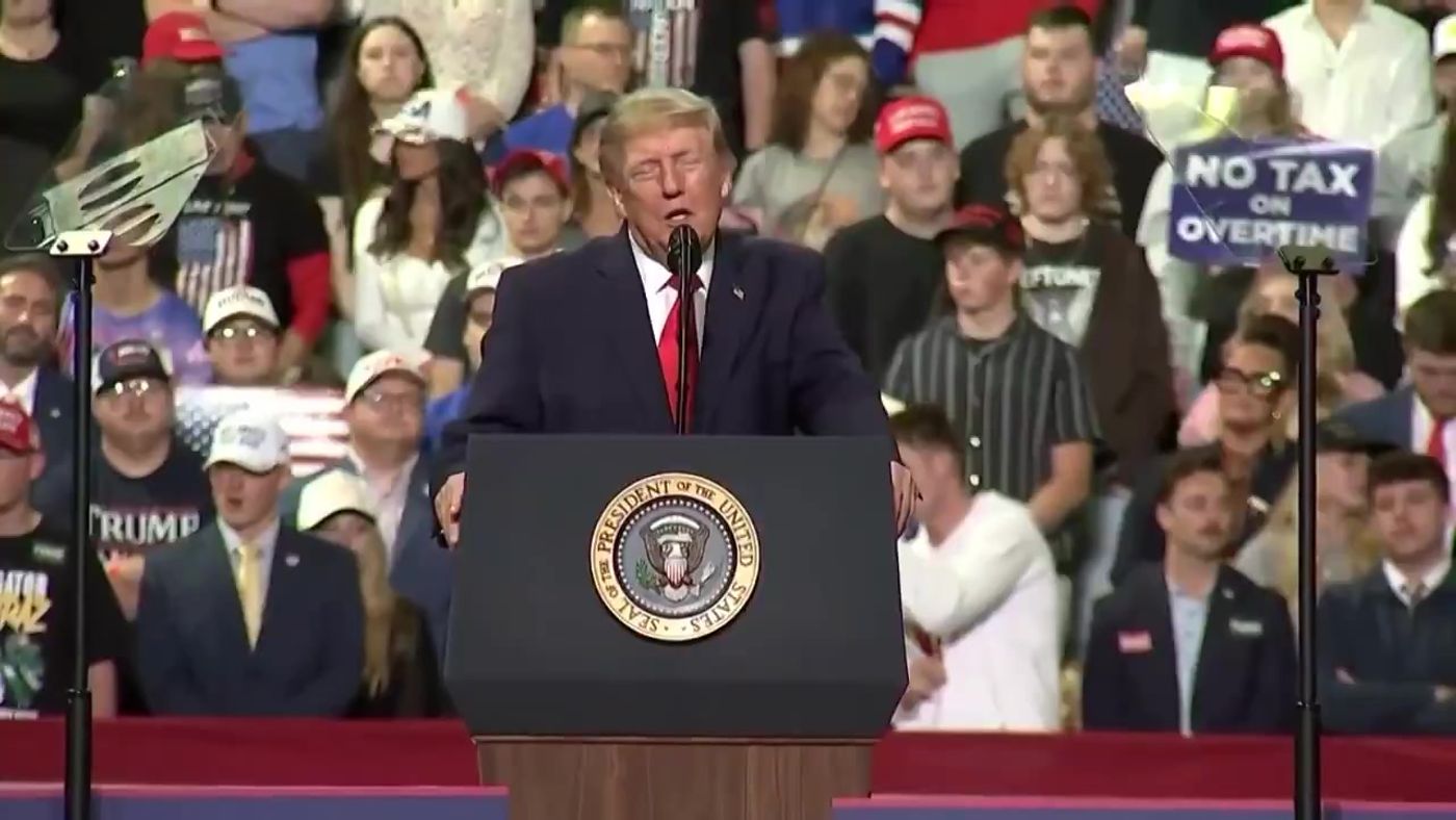 President Trump at the Youngstown rally podium with a NO TAX ON OVERTIME sign visible, October 12, 2026 (still from Rapid Response 47 video)
