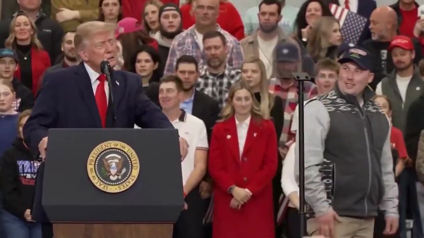 President Trump speaks at a podium bearing the presidential seal as a man in a cap stands on stage nearby at his rally in Wasilla, Alaska, October 13, 2026 (still from Rapid Response 47 video)