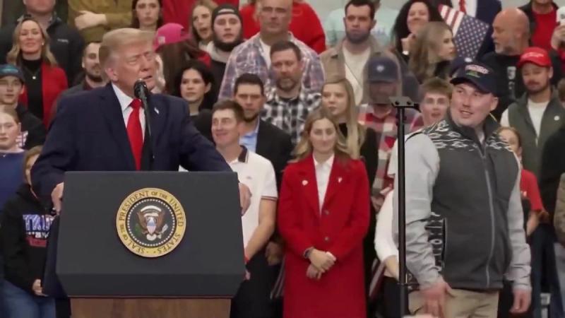 President Trump speaks at a podium bearing the presidential seal as a man in a cap stands on stage nearby at his rally in Wasilla, Alaska, October 13, 2026 (still from Rapid Response 47 video)