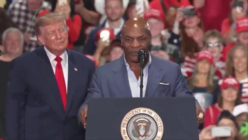Mike Tyson speaks at the presidential lectern as President Trump stands beside him on stage at his rally in Syracuse, New York, October 9, 2026 (still from Official White House video)