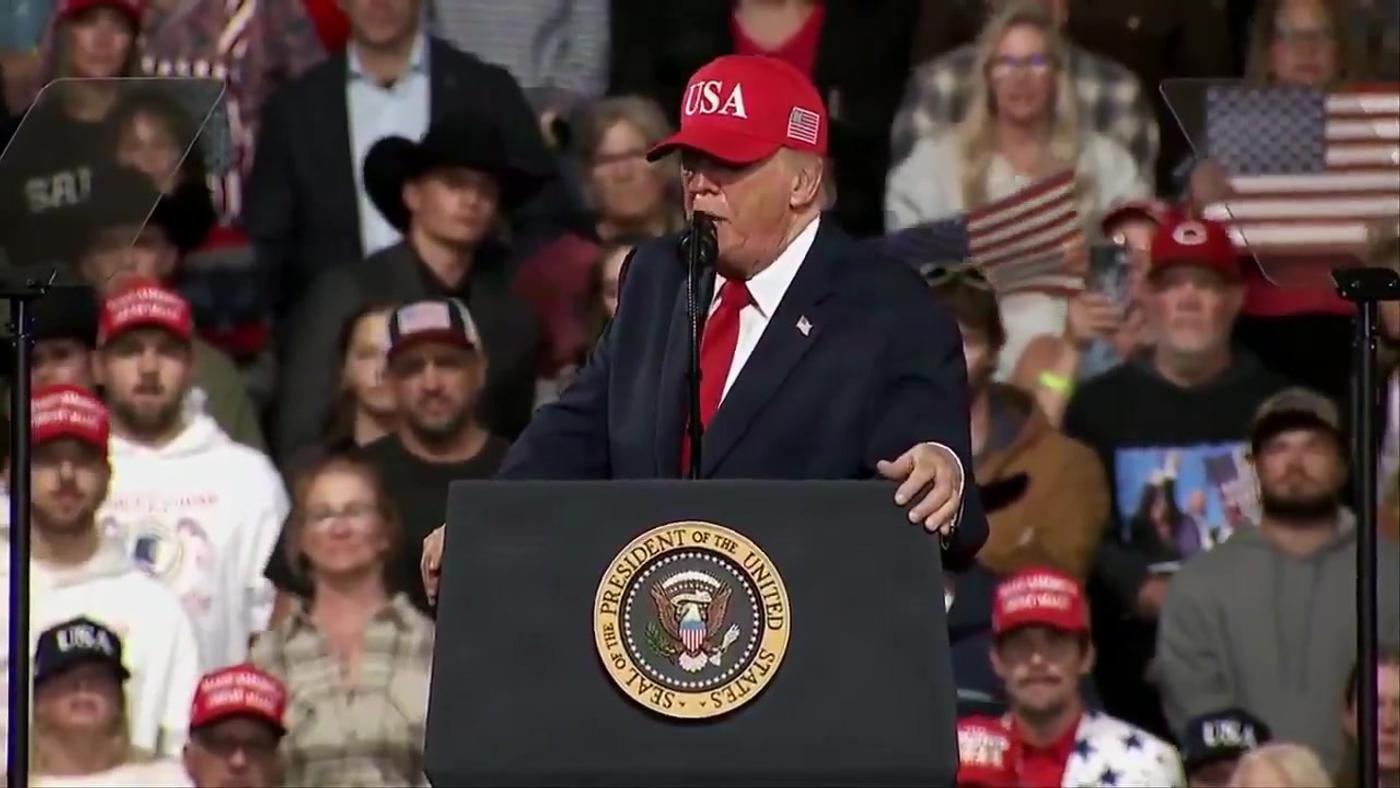 President Donald J. Trump, wearing a red USA cap, speaks at a lectern bearing the presidential seal at his rally in Montana, October 14, 2026 (still from Rapid Response 47 video)