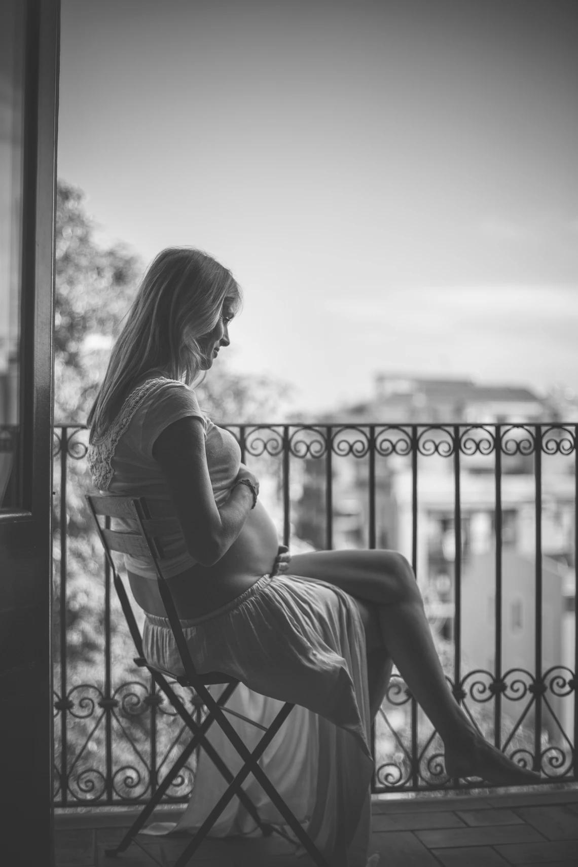 Pregnant woman sitting peacefully on a balcony, hands on belly.