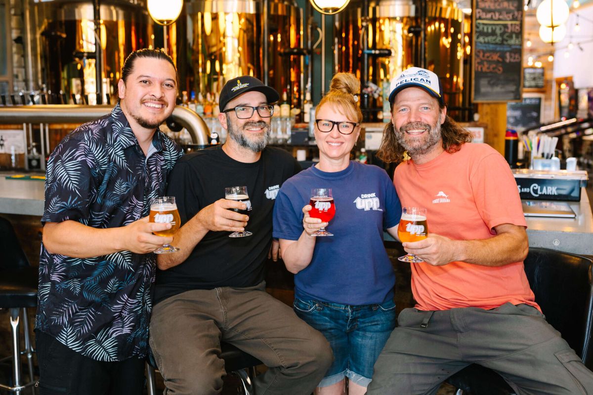 Four UPP Liquids brewers holding beer glasses in front of copper tanks at their Bend taproom.
