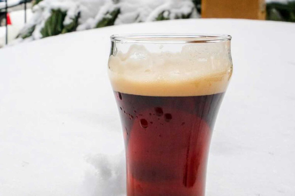 A glass of Northbound Eisbock standing in snow with evergreens behind it.