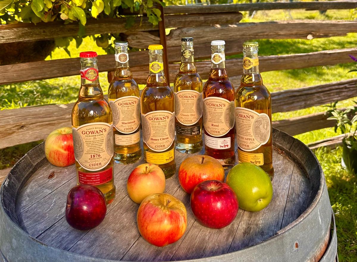 Gowan's cider bottles and apples on a barrel in the orchard, with Honey Citron third from the left.