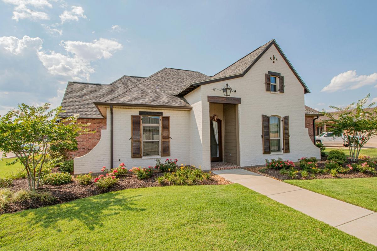 Single-story white brick home with dark shutters, landscaped flower beds and a front lawn