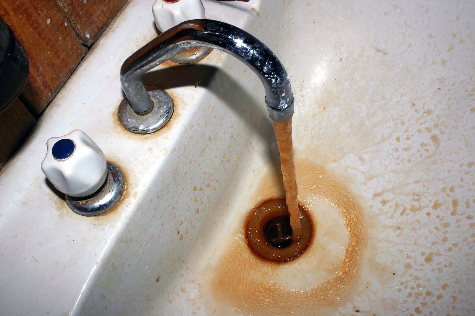 Rusty brown water running from a faucet and staining a white sink