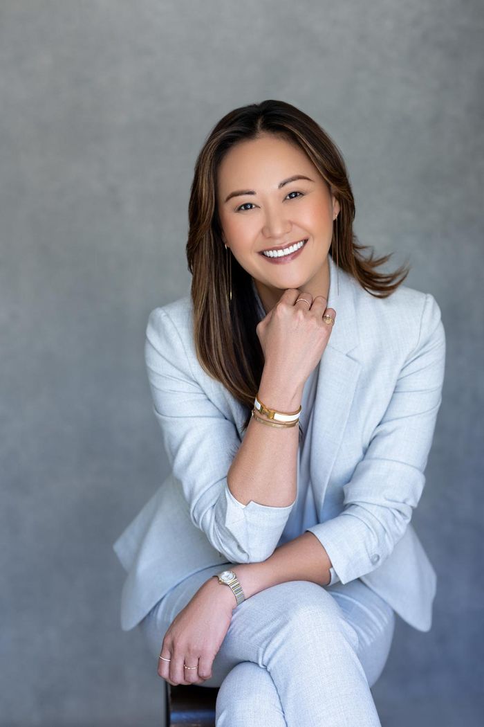 Christina Kim in a pale blue suit, seated, resting her chin on her hand and smiling