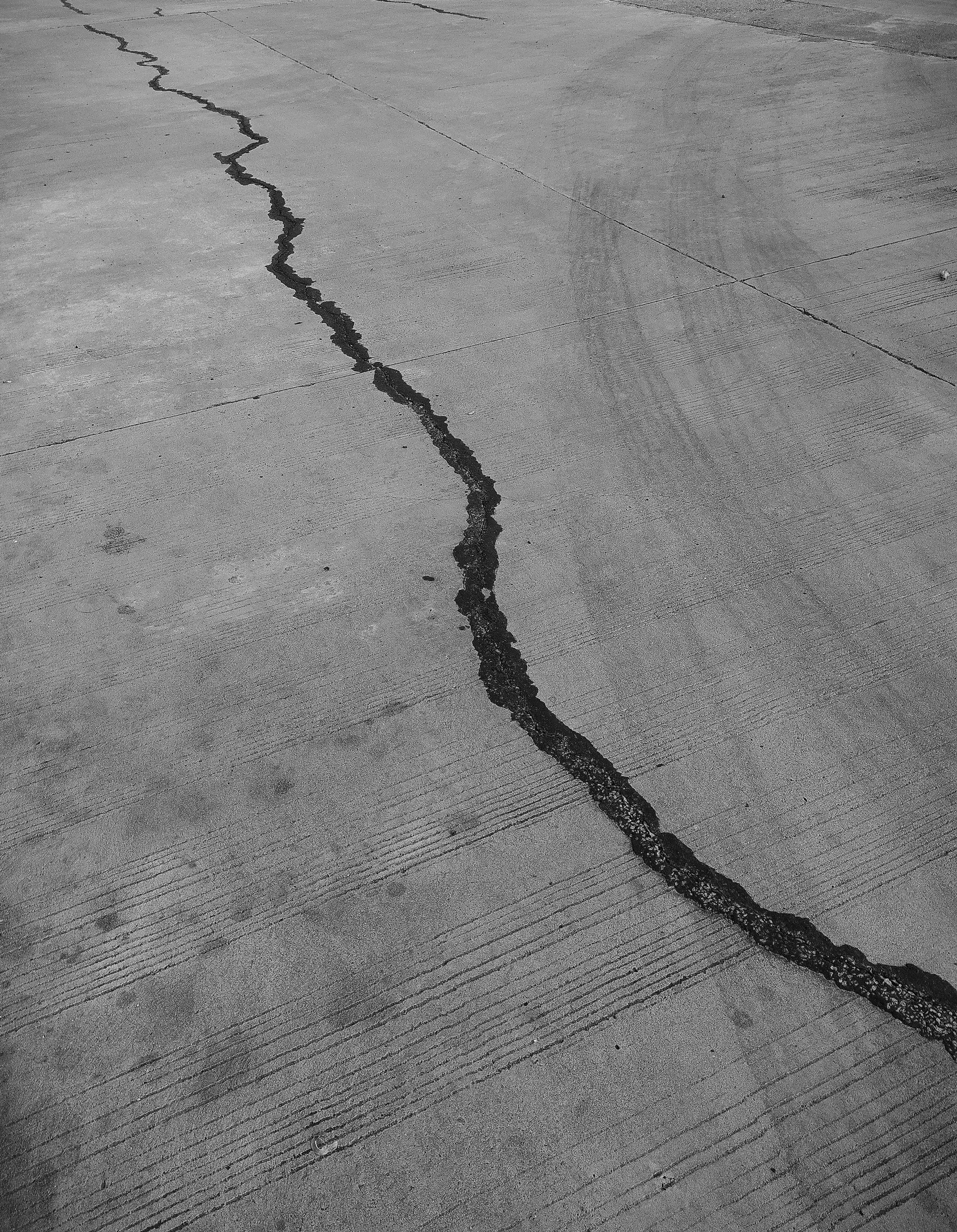 Long jagged crack running across a concrete surface, evoking earthquake damage