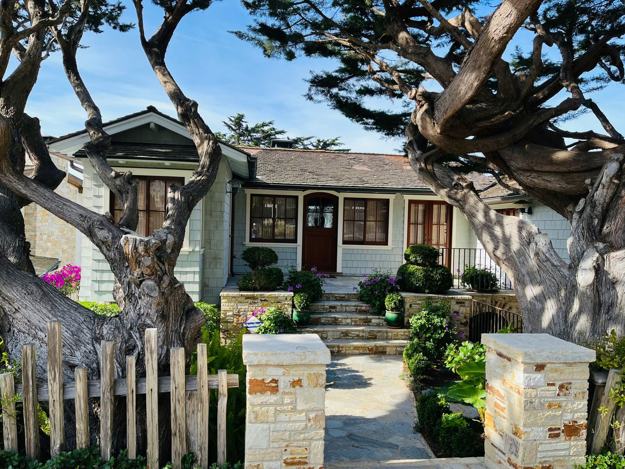Craftsman cottage behind a stone gate framed by twisting cypress trees