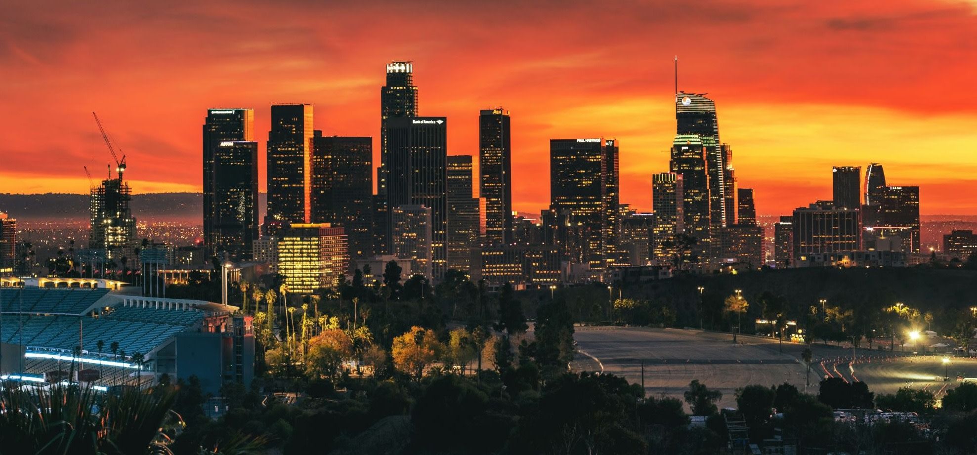 Downtown Los Angeles skyline silhouetted against a fiery orange sunset