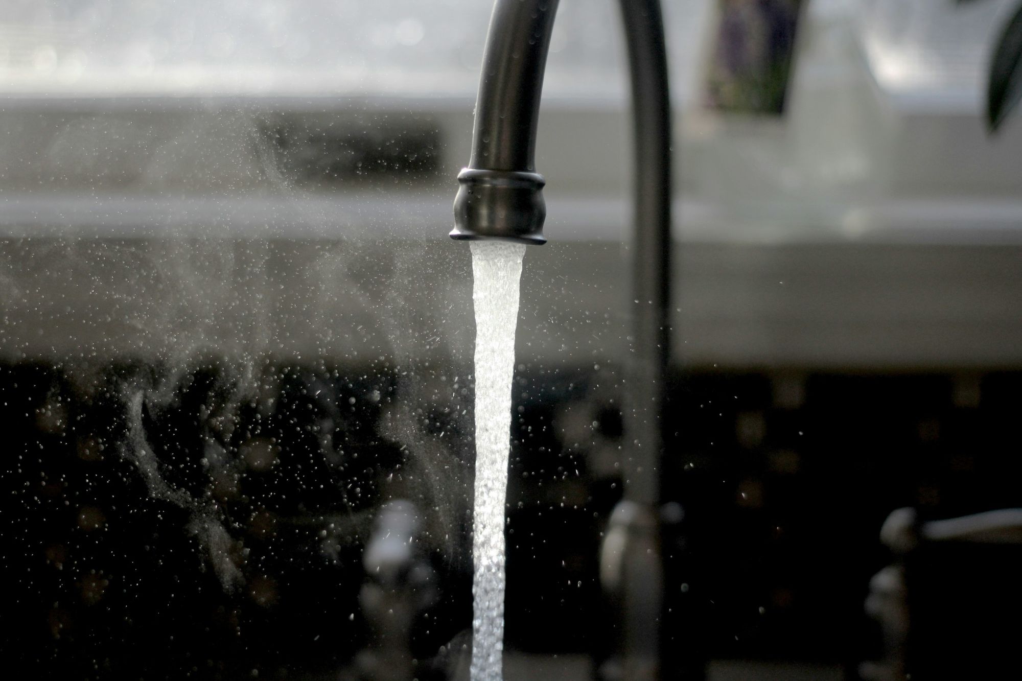 Stream of water pouring from a dark kitchen faucet