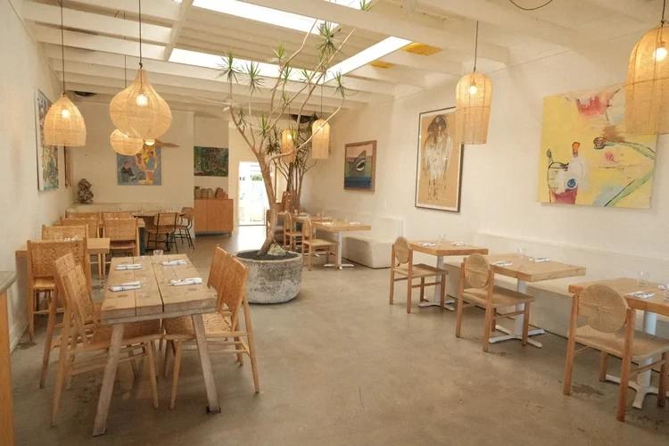 Airy restaurant dining room with wooden tables, woven pendant lamps and an indoor olive tree