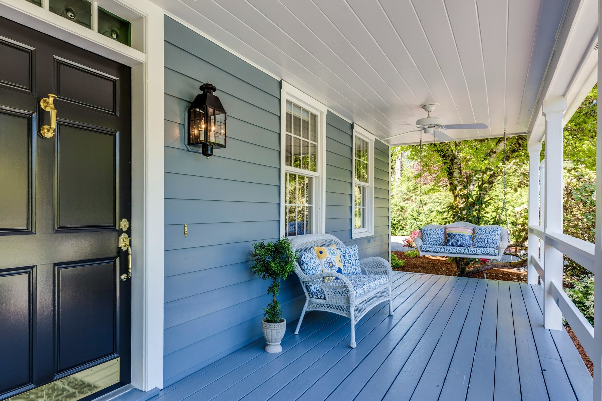 Front porch with a black door, white wicker bench and hanging porch swing