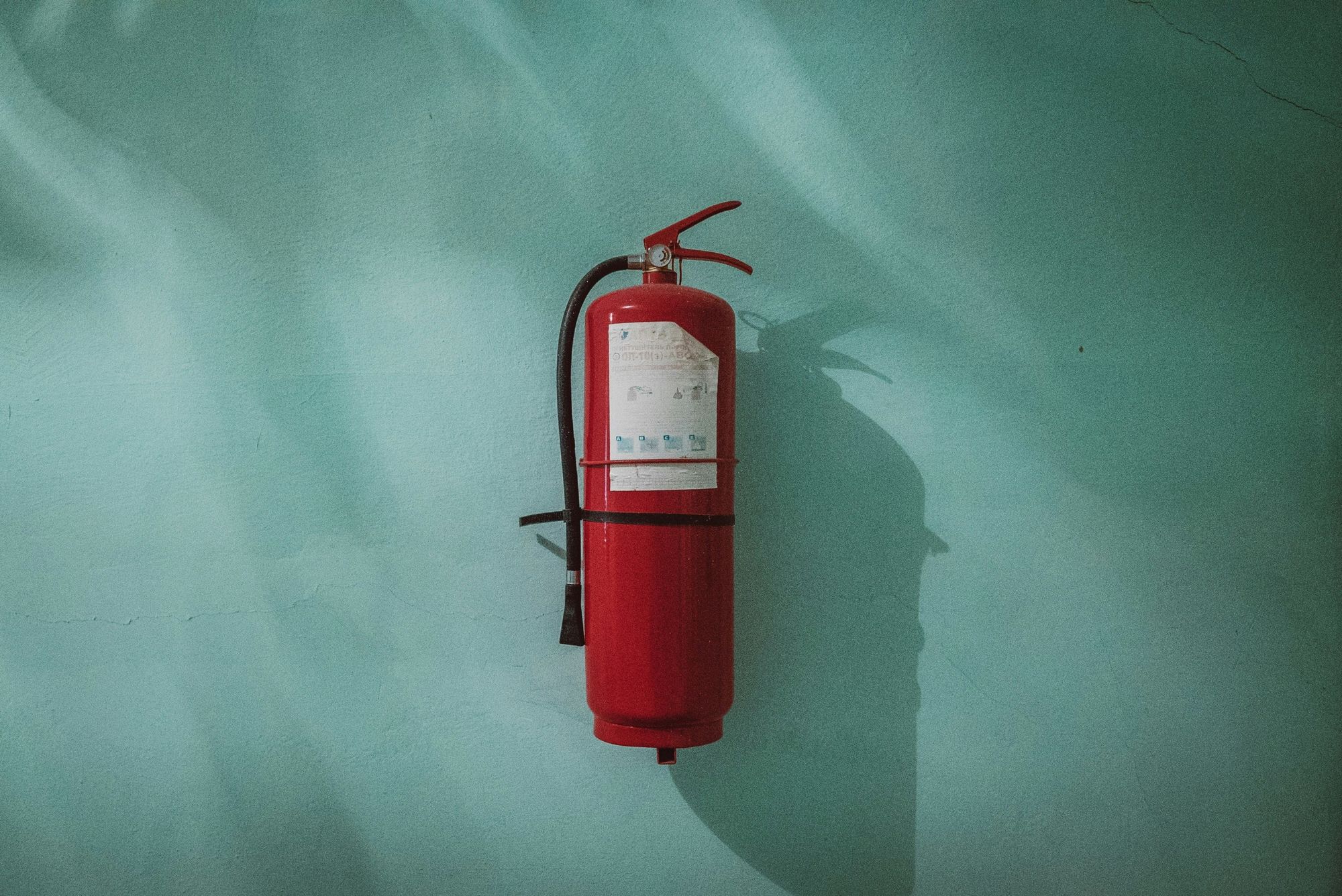 Red fire extinguisher mounted on a pale teal wall