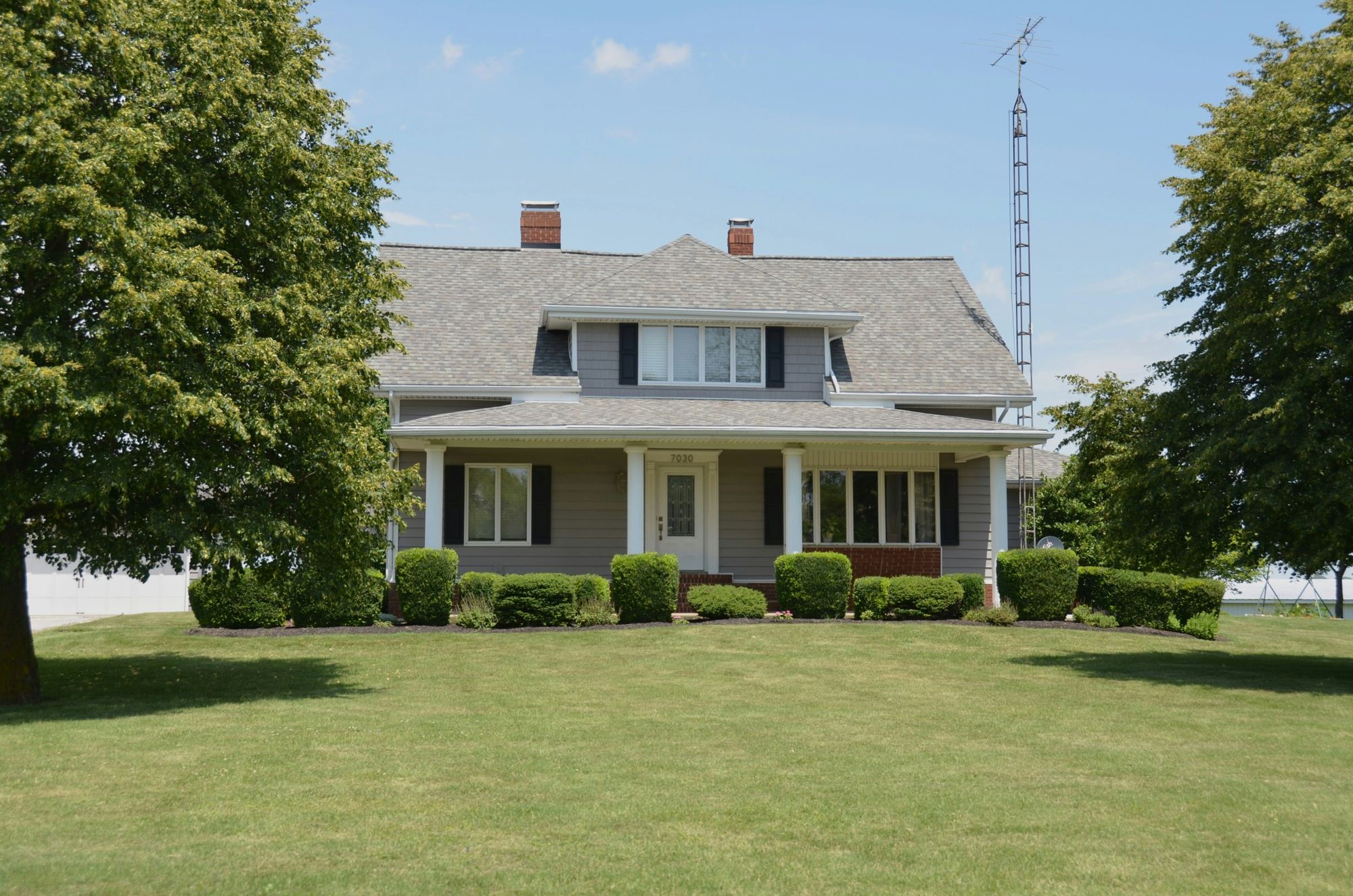 Two-story grey farmhouse with a covered front porch and wide green lawn
