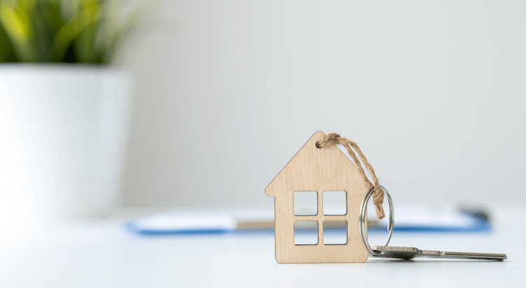 Wooden house-shaped keychain with a key resting on a white desk