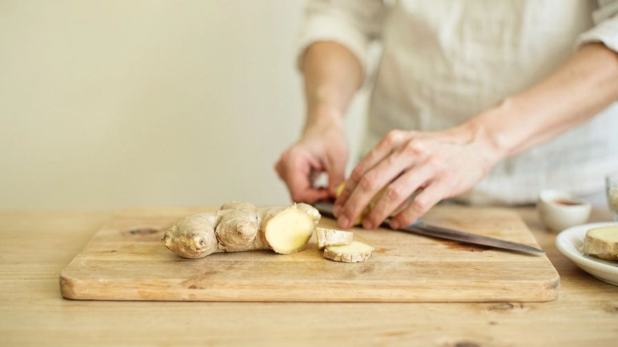 Una radice di zenzero parzialmente affettata su un tagliere di legno.