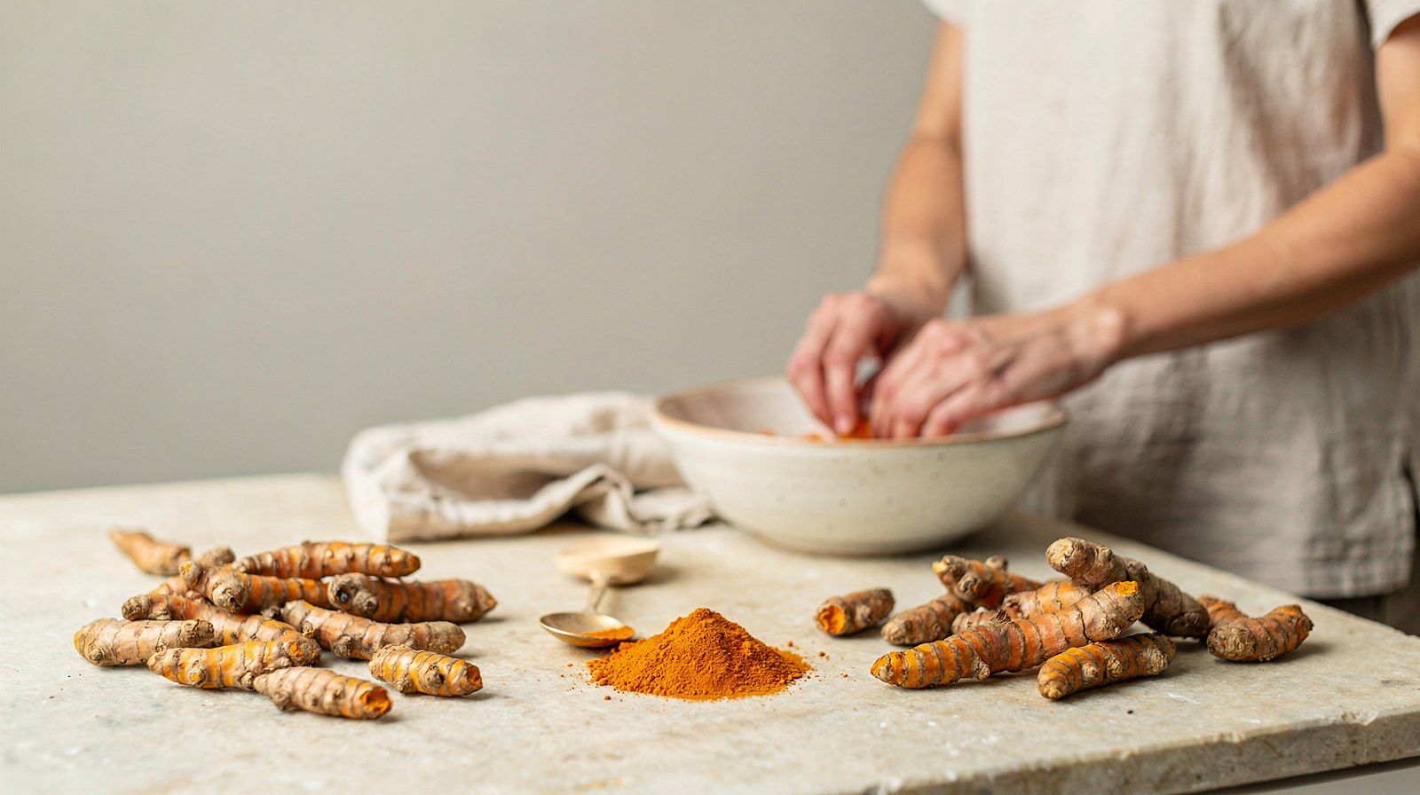 Radici fresche di curcuma e un cucchiaio di curcuma in polvere.