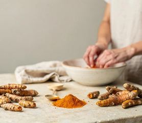 Radici fresche di curcuma e un cucchiaio di curcuma in polvere.