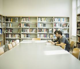 Una sala di lettura luminosa con scaffali alti e un lungo tavolo vuoto.