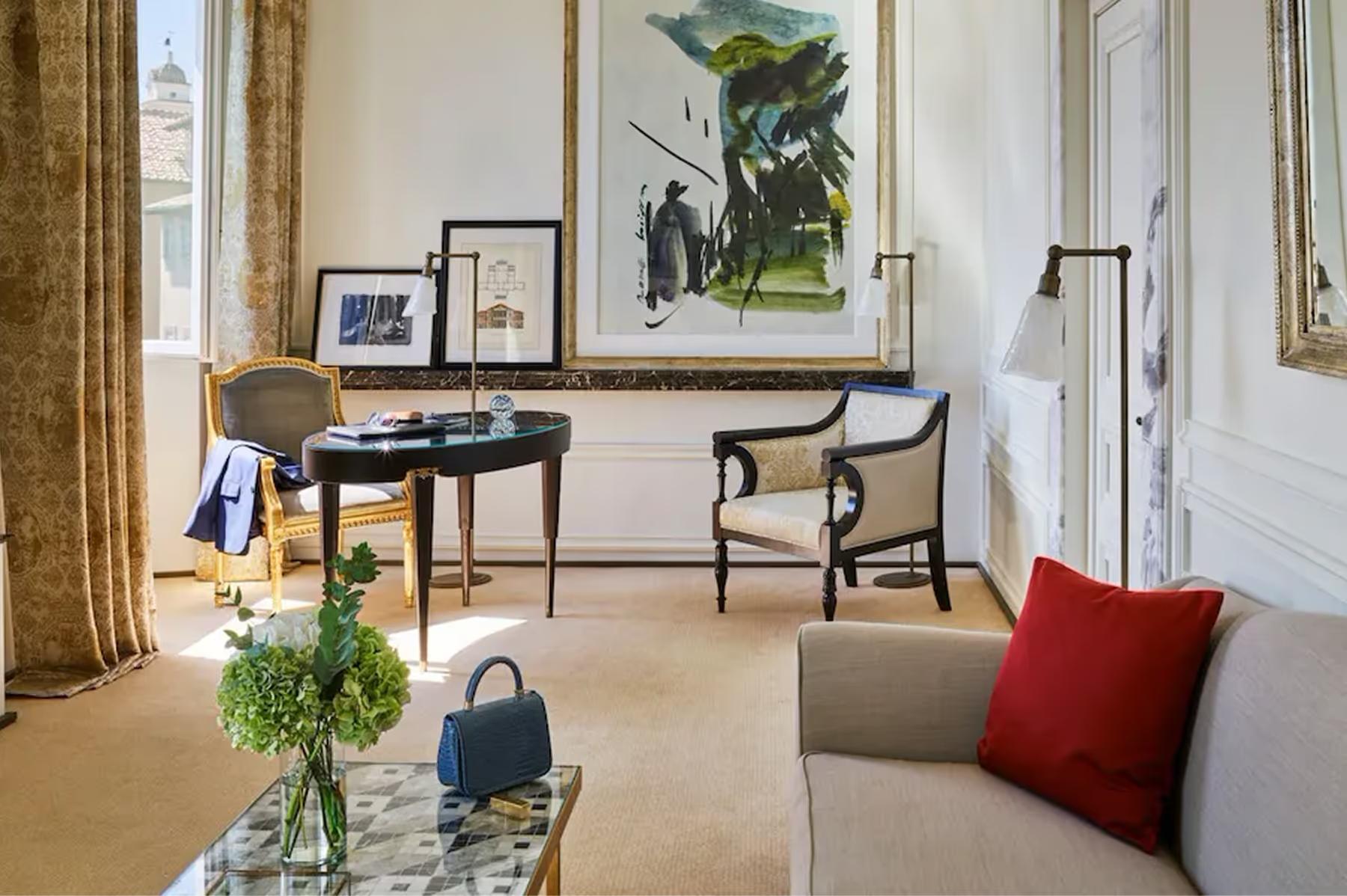 Hotel Eden: a suite with a desk, sitting area with red accent pillows, artwork, and tall windows with gold drapery