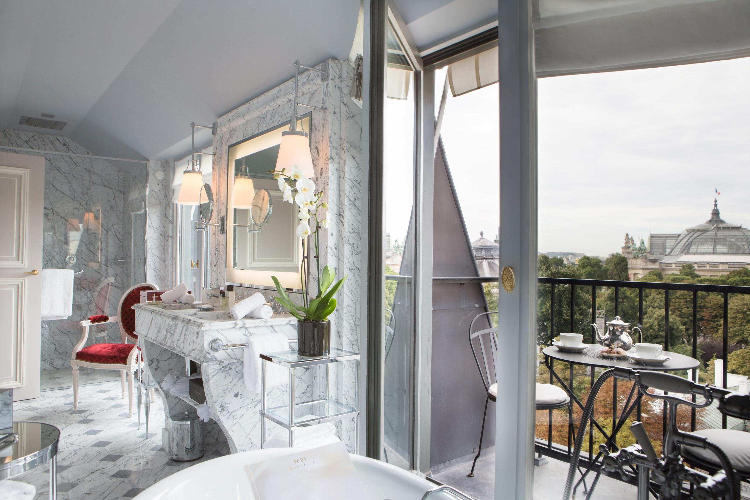A bathroom with white marble, a red accent wall, and a mirrored vanity with Paris rooftop views