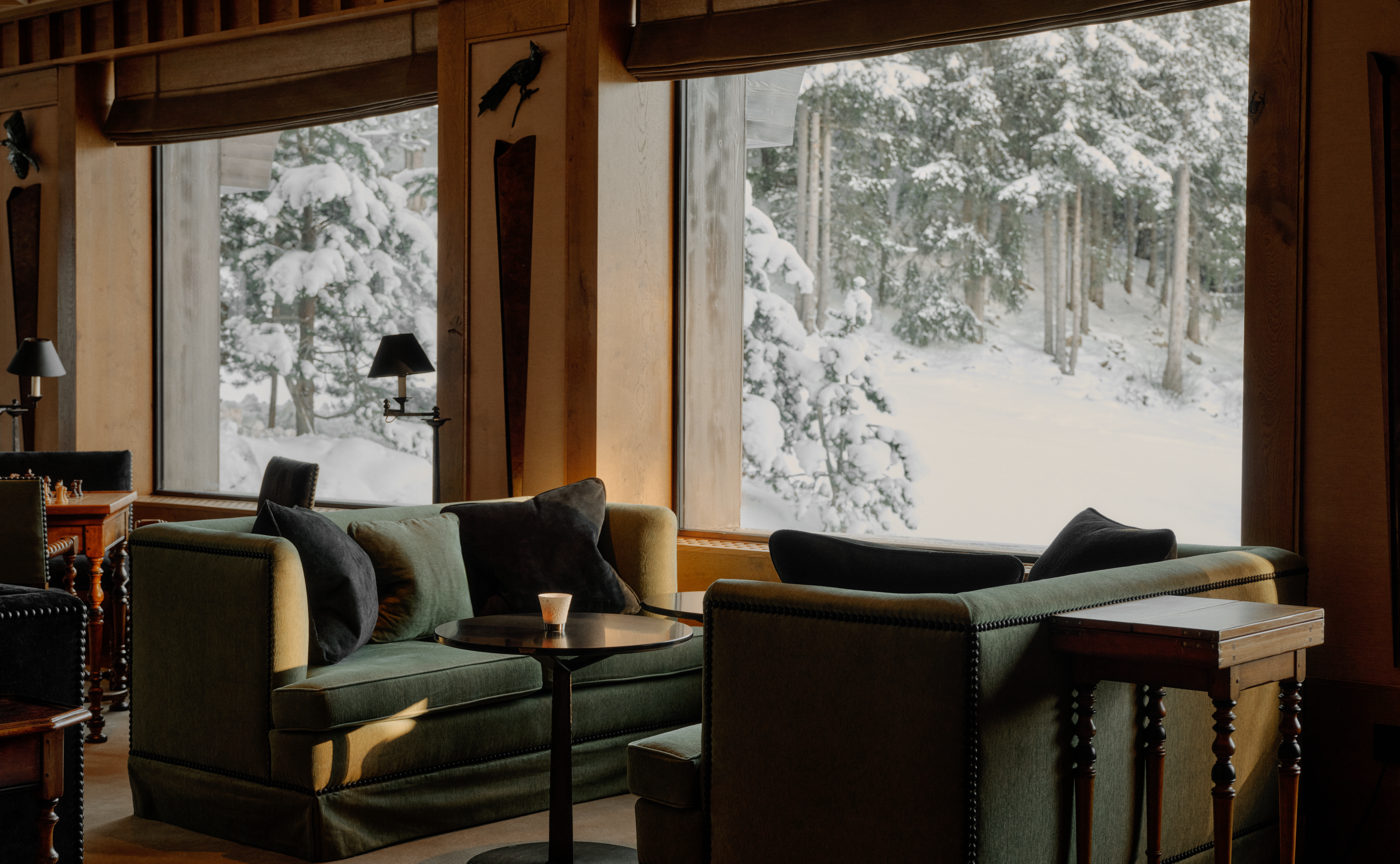 A lounge at Aman Le Mélézin with deep green sofas and windows onto snowy forest