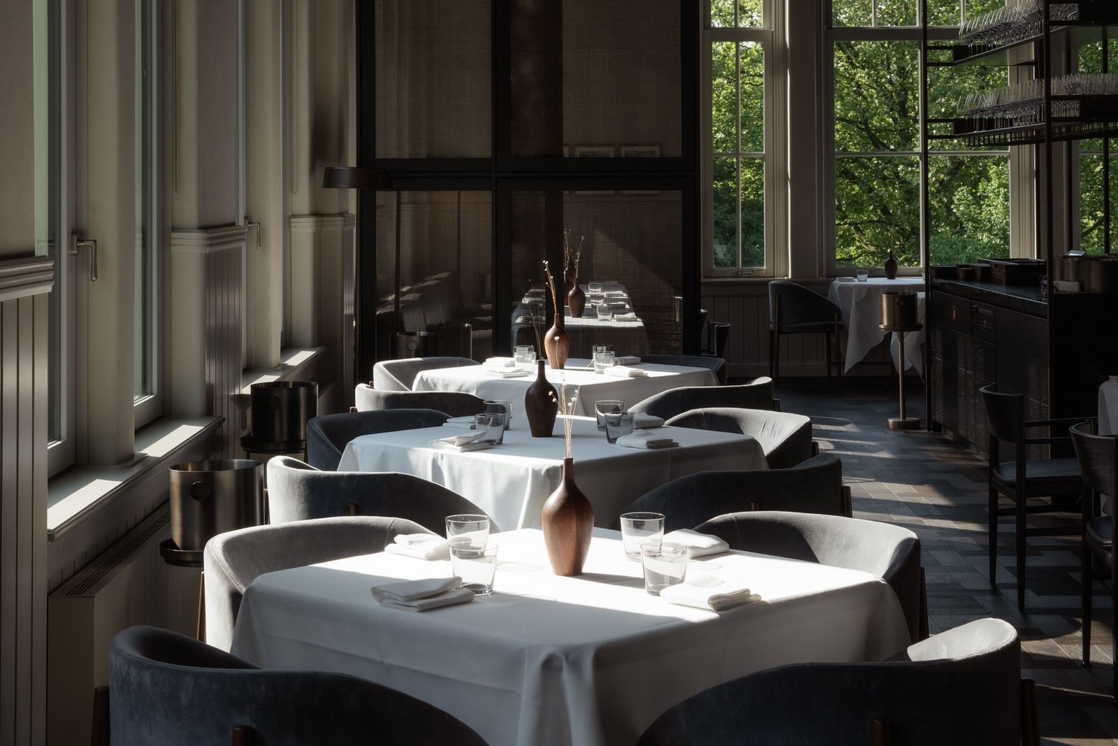White-clothed tables in the VanOost dining room at Pillows Maurits at the Park, trees in the tall windows