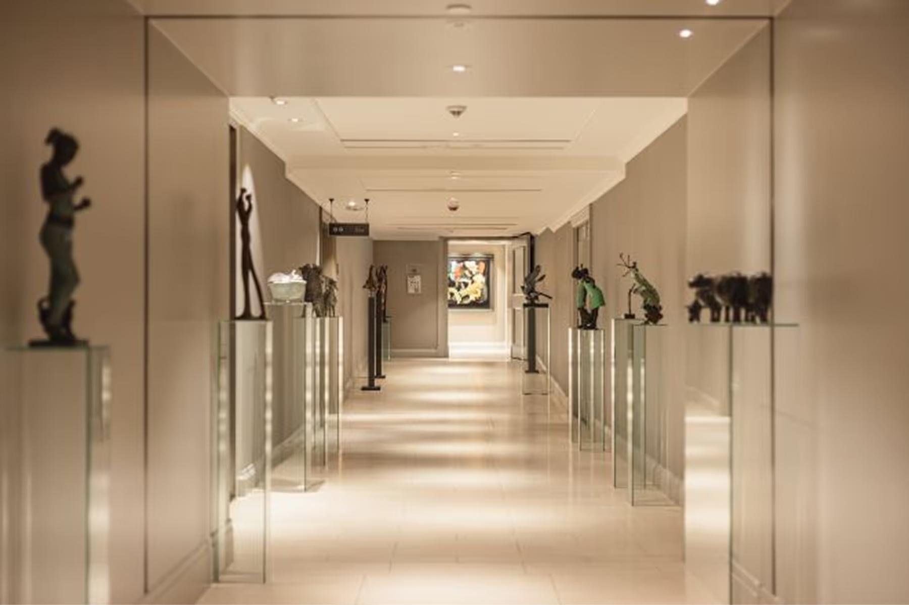 A corridor with glass railings, sculptural pieces displayed on shelves, and soft ambient lighting