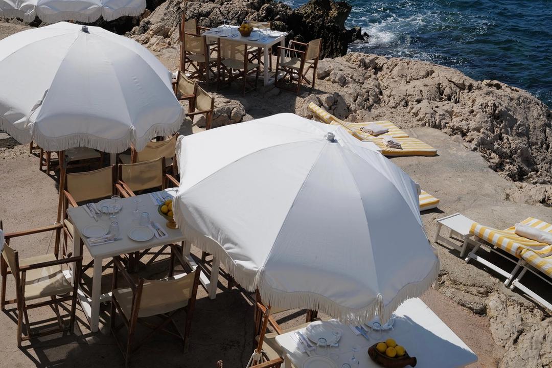 White parasols and canvas chairs set out on the rocks at Tuba Club, the sea beyond