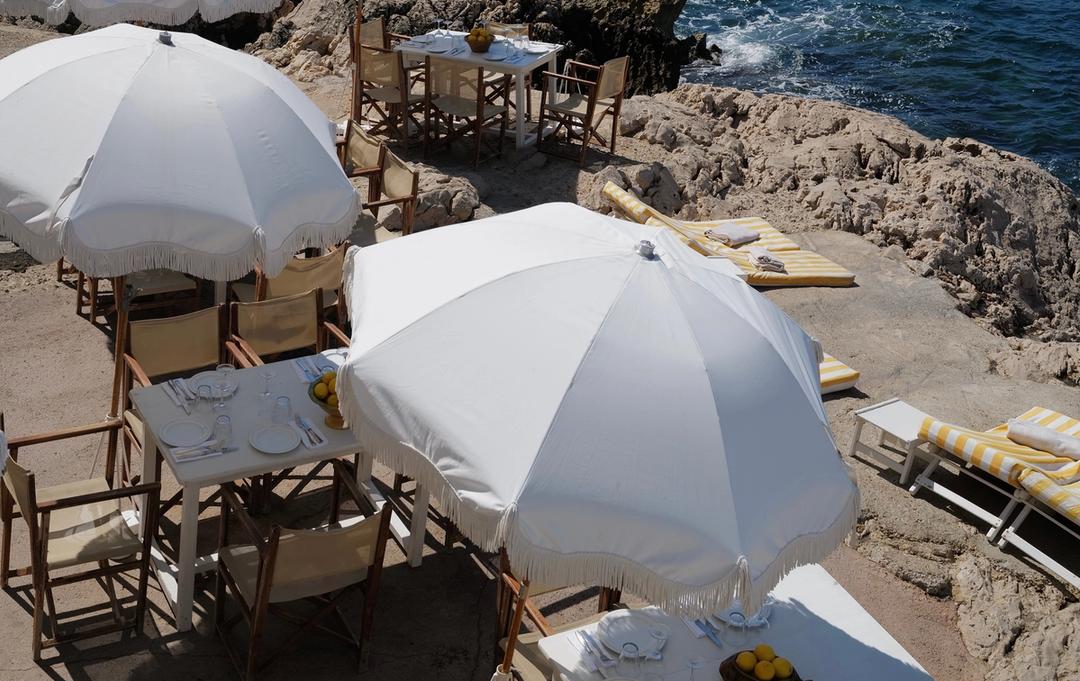 White parasols and canvas chairs set out on the rocks at Tuba Club, the sea beyond