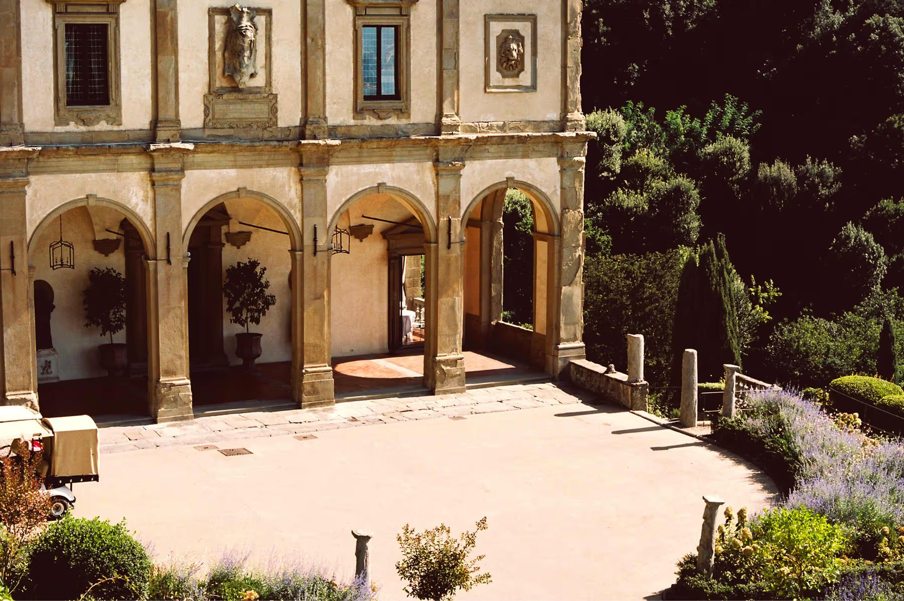 Villa San Michele: vaulted courtyard with arched openings, dark wooden doors, terracotta flooring, and cypress beyond