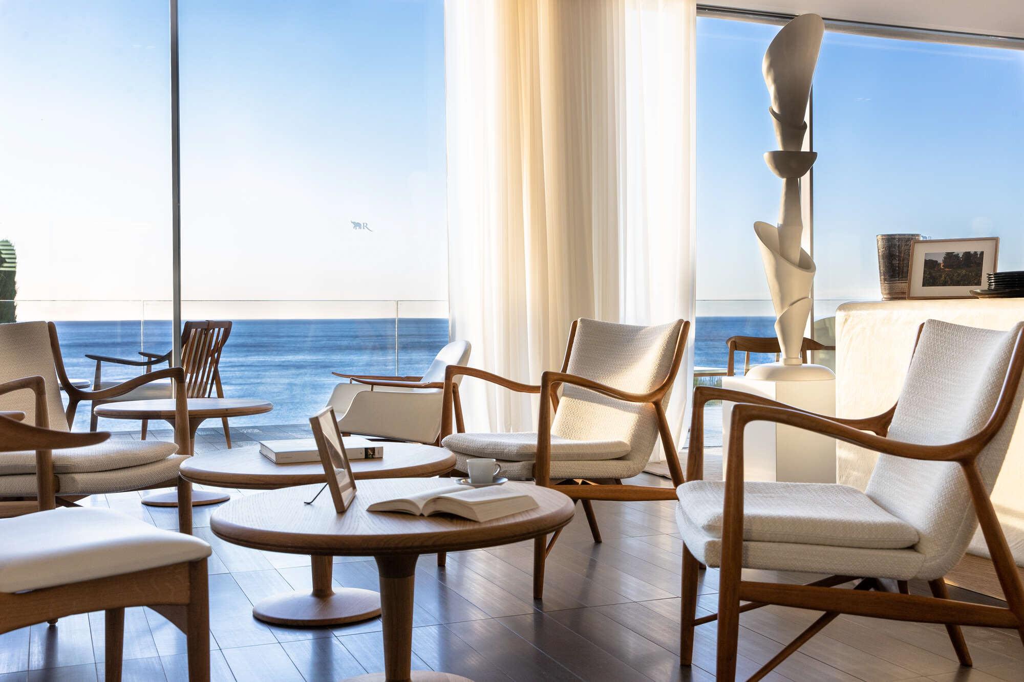 Light-filled lounge with woven chairs and sea views through glass doors