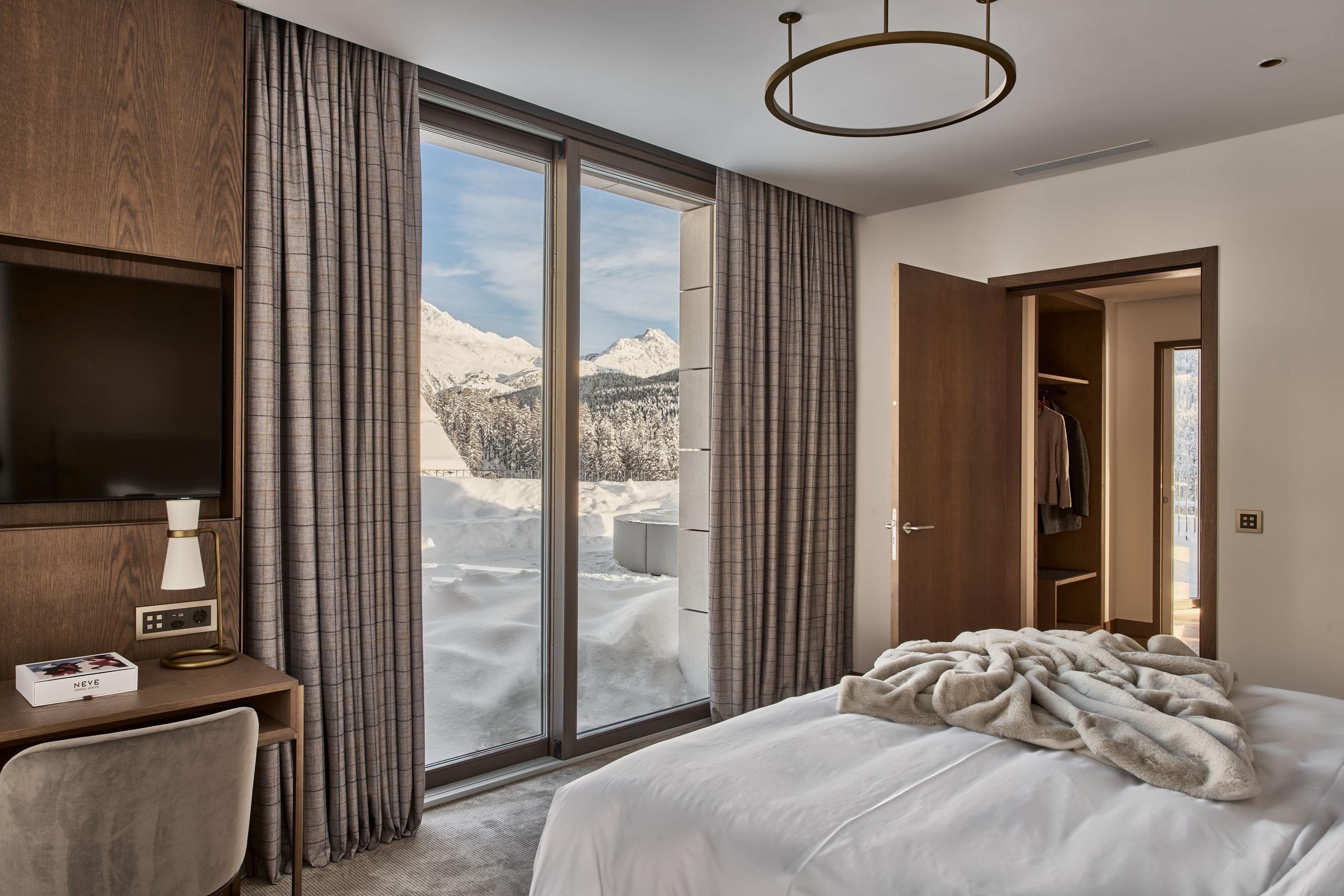Bedroom with brown wood accents, tan bedding, glass doors opening to balcony views