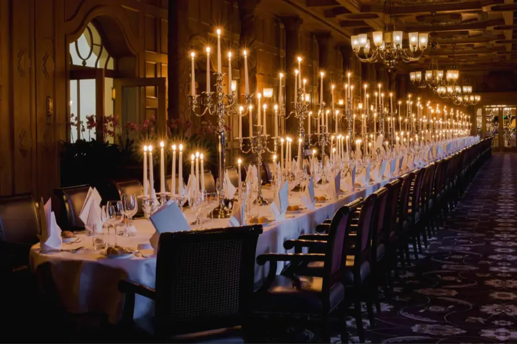Suvretta House: a long banquet hall with row of hanging pendant lights and formally set tables with white linens