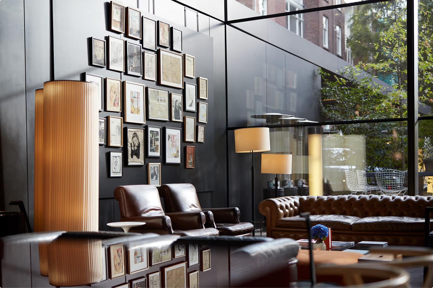 Mandarin Oriental Conservatorium, Amsterdam: lounge with buttoned leather sofas and armchairs, tall lamps, and a wall of framed pictures beside a glass facade