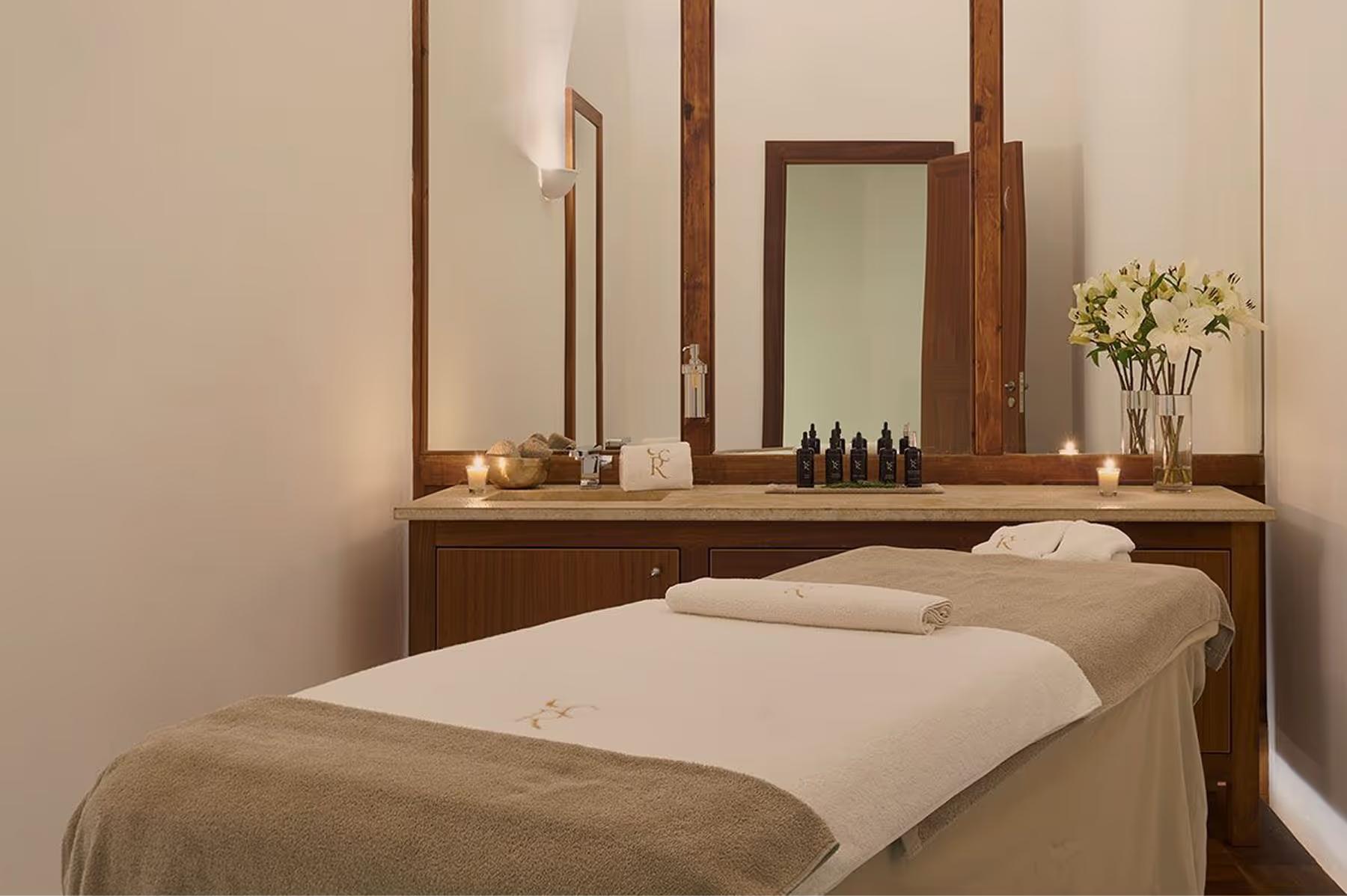 A massage room with a treatment table, mirror, white orchids, and warm natural light