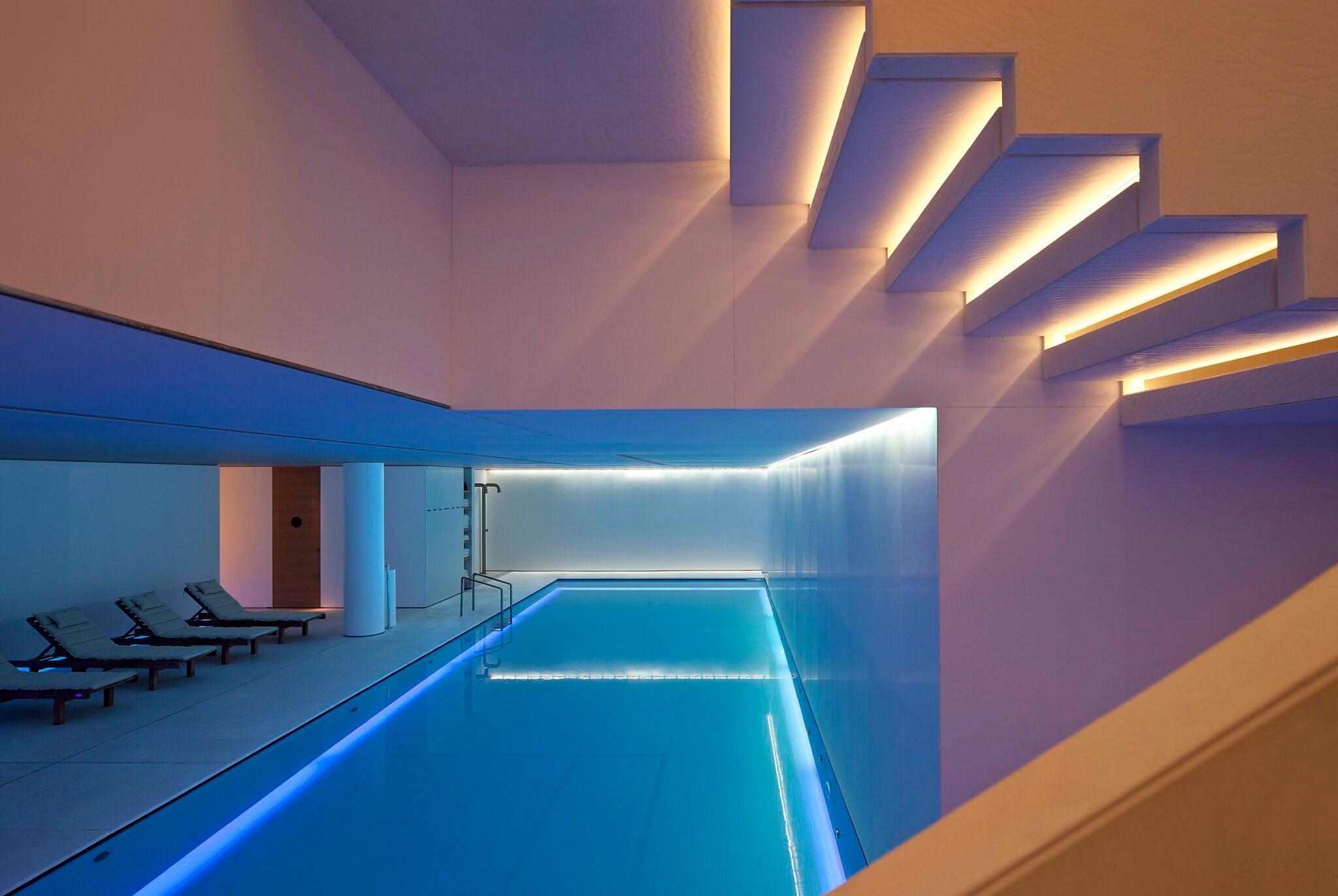 Mandarin Oriental Conservatorium, Amsterdam: indoor pool lit in blue, with loungers along one side and a staircase with lit steps above