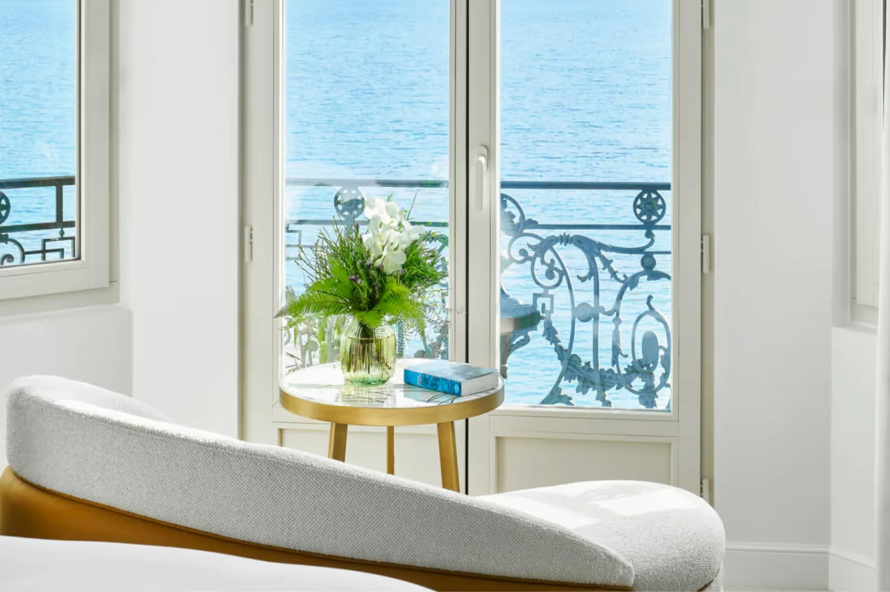 Carlton Cannes: window nook with white upholstered seating overlooking the sea, with white-painted French doors and a tall plant