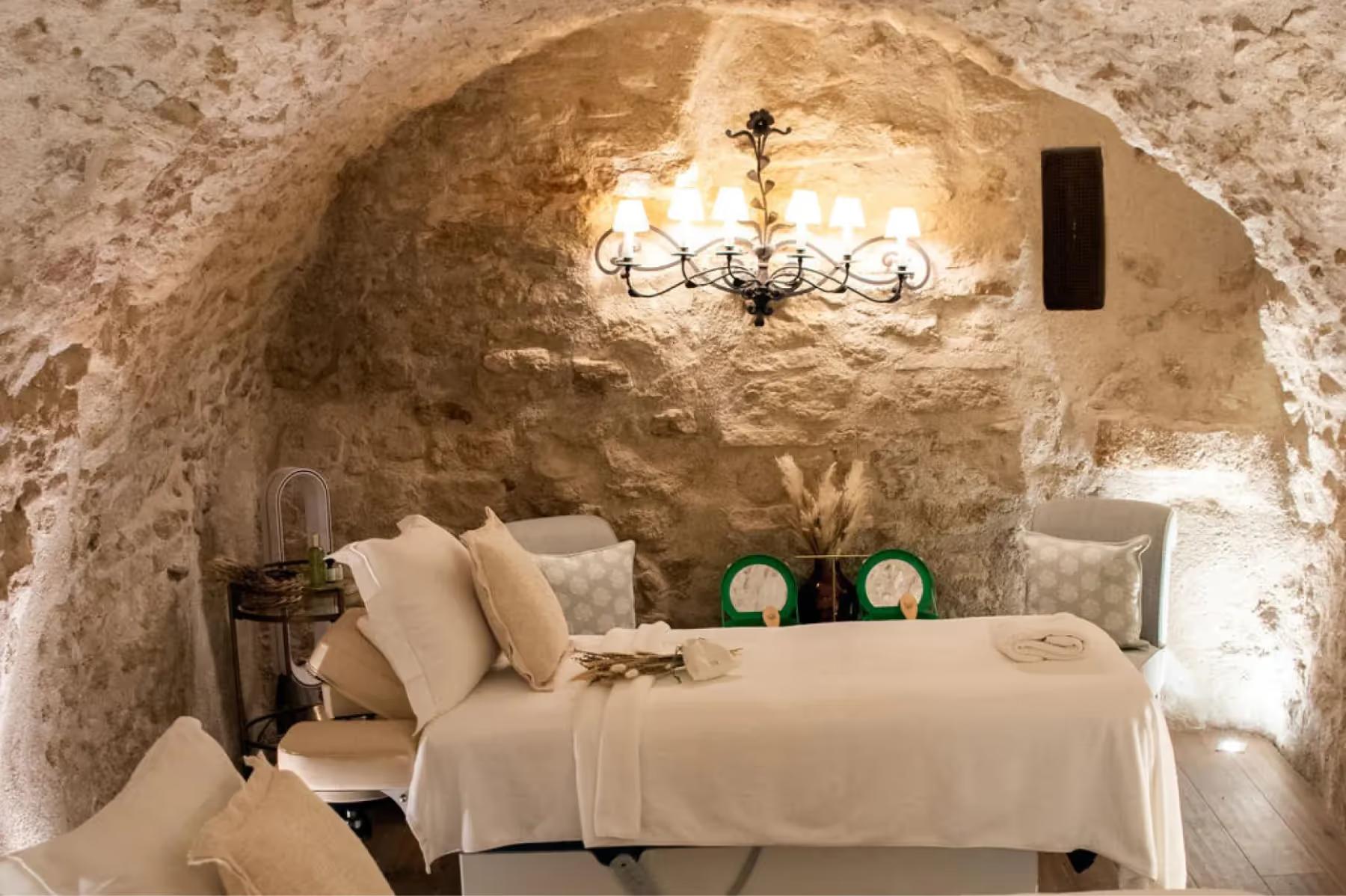 A spa treatment room carved into stone with arched ceiling, massage table, and soft ambient lighting