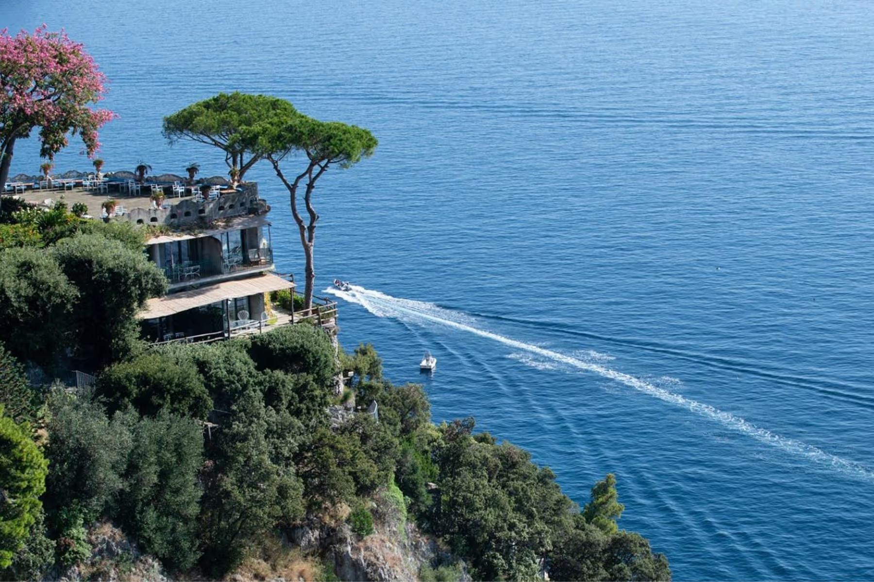 Cliffside building above Mediterranean water with native vegetation and umbrella pines