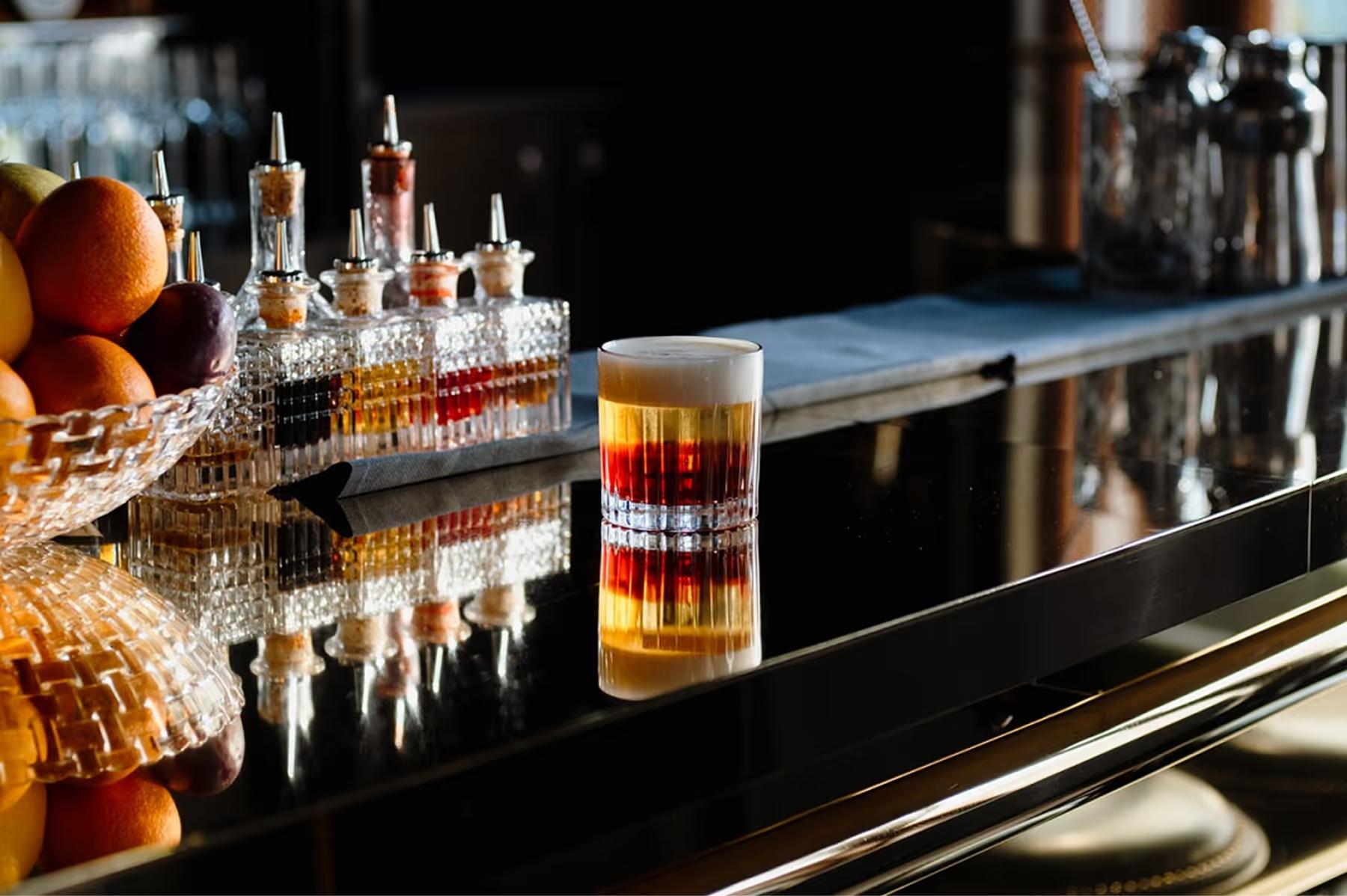 De L’Europe Amsterdam: cocktail bar with dark surface, bottles, and single glass with spirits
