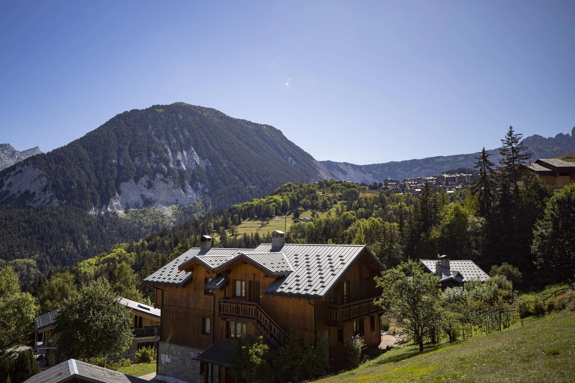 A timber chalet below green summer peaks at Courchevel