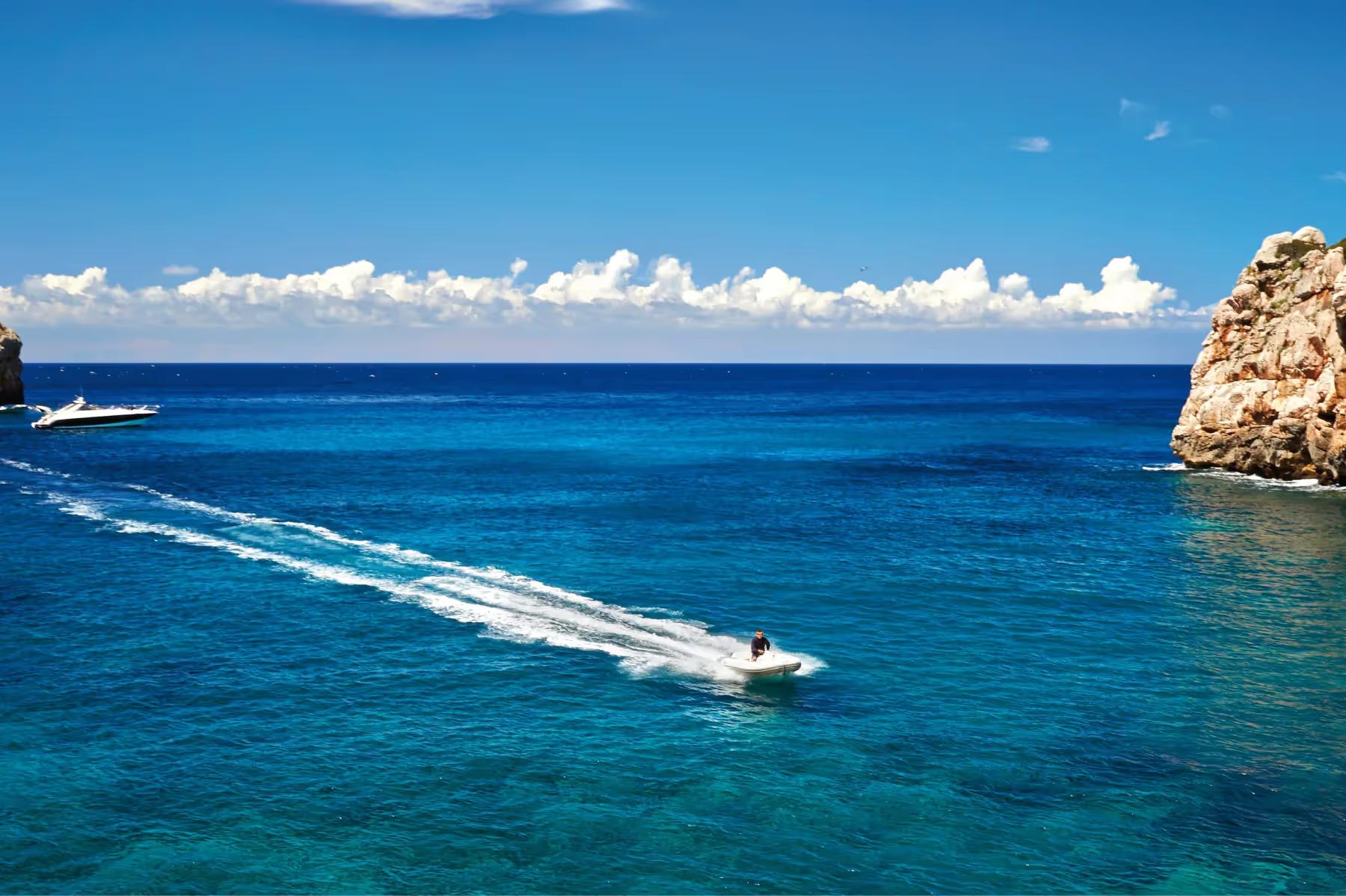 La Residencia: boat traveling on turquoise Mediterranean water with rocky coastline and clear sky