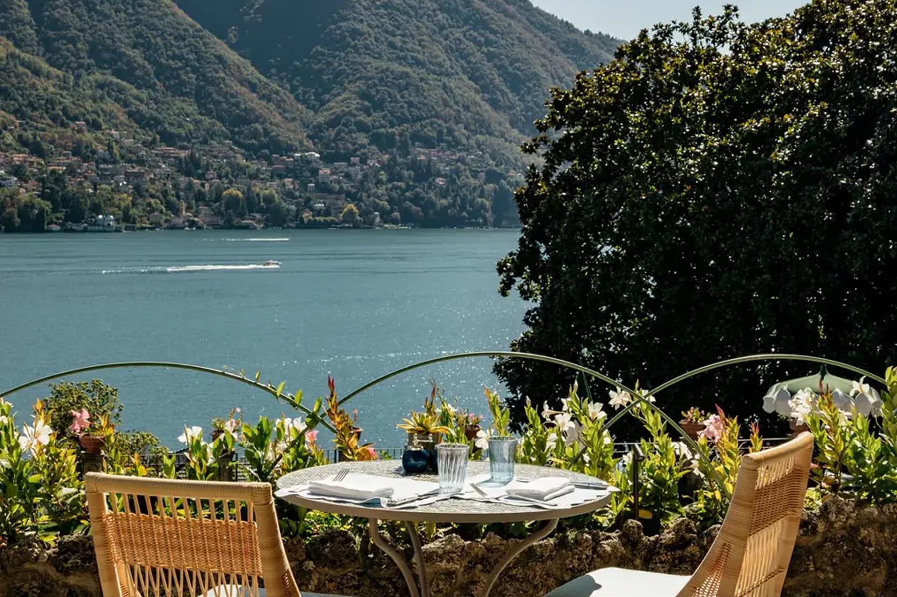 Passalacqua: a terrace table with lake and mountains visible beyond flowering potted plants