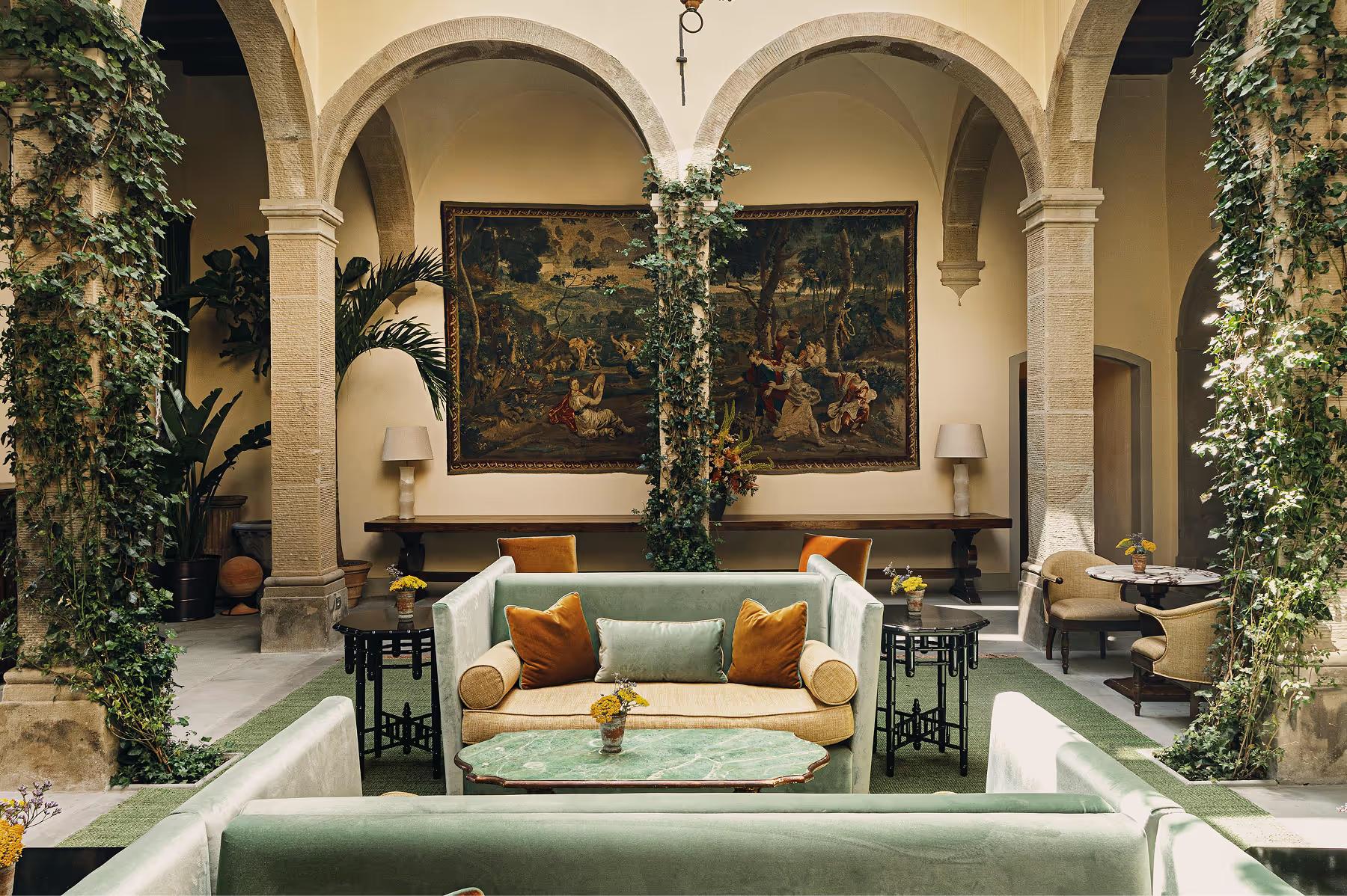 Villa San Michele: grand vaulted courtyard with cream sofa, orange cushions, climbing ivy, arches, and Old Master paintings