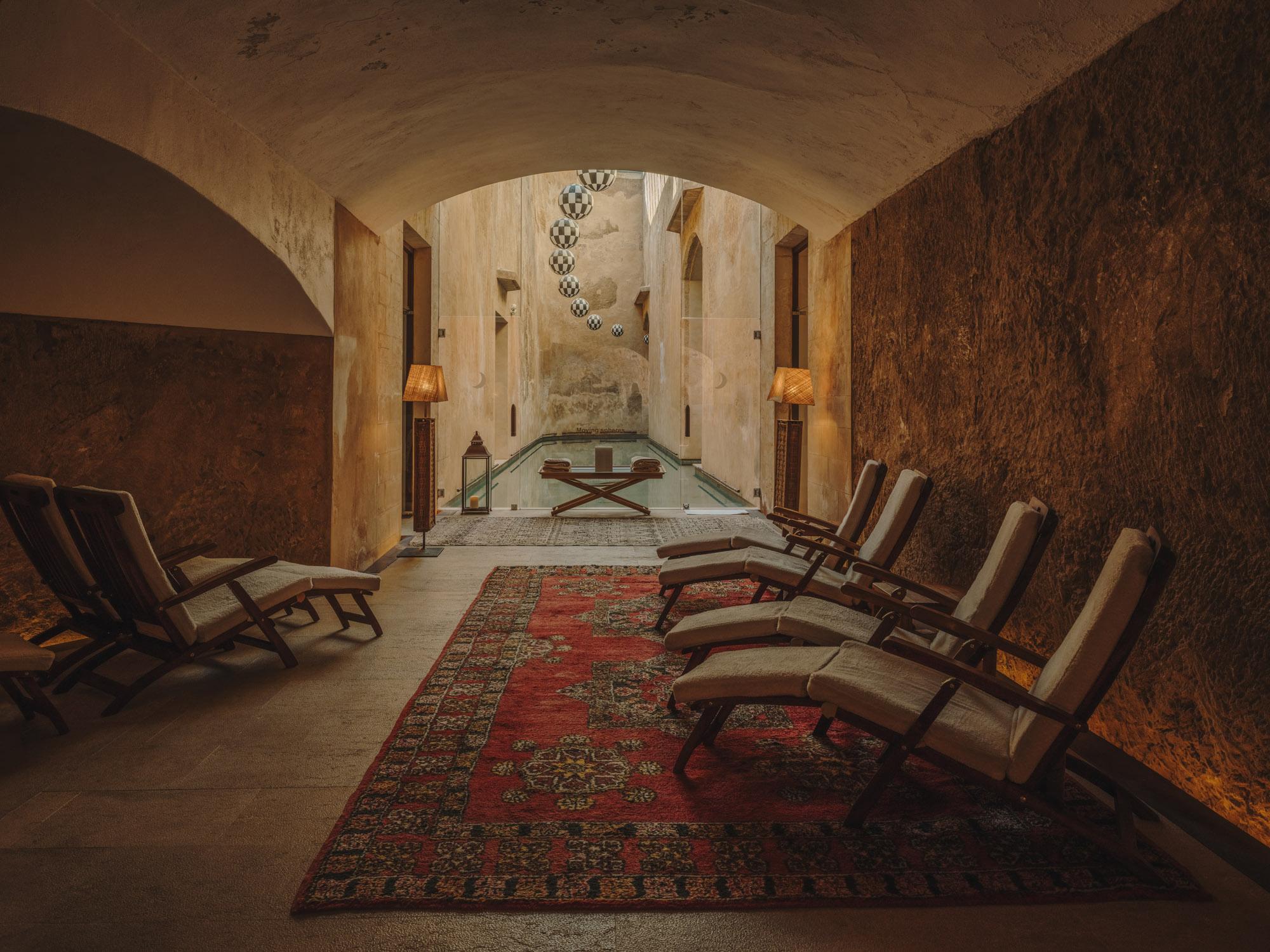 A stone hammam interior with arched ceilings, olive-toned walls, and centered relaxation spaces